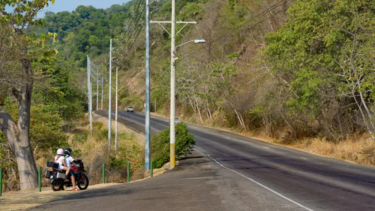Man sieht eine Landstraße. Aus einer Einfahrt möchte ein Motorrad einbiegen.