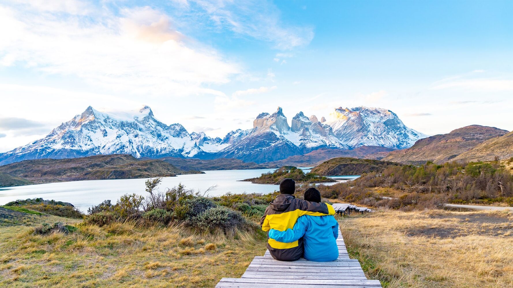 Ein Paar sitzt Arm in Arm auf einem Steg. Im Hintergrund das Bergpanorama vom Torres del Paine